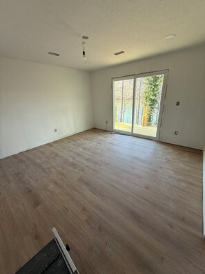 Una habitación amplia con un gran ventanal corredero que da a un espacio exterior, suelo de madera e iluminación empotrada en el techo.