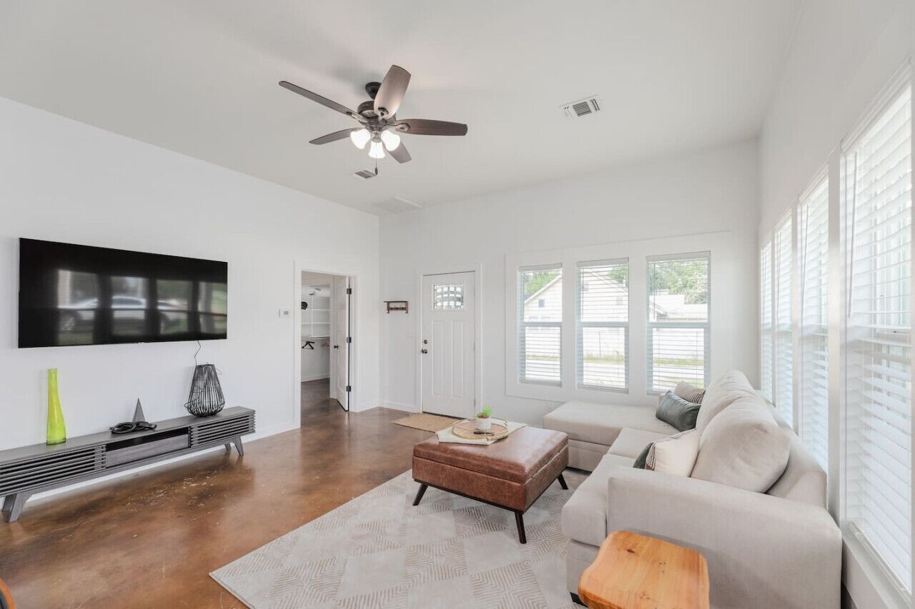 A spacious living room with a ceiling fan, a large flat-screen TV, a sofa, and a coffee table.