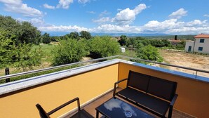 Ein Balkon mit Tisch und Stühlen mit Blick auf eine ländliche Landschaft mit Bäumen und Gebäuden.