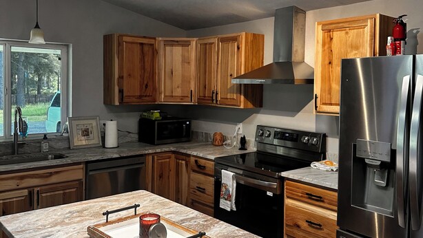 Une cuisine moderne avec des meubles en bois, un réfrigérateur en acier inoxydable et une lucarne au-dessus de l’îlot central.