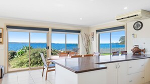 A kitchen with large sliding glass doors, a central island, white cabinets, and a view of the sea. - Ocean's Edge in Batehaven (Batehaven)