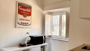Een keuken met witte kastjes, een magnetron en een poster van Campbell's Vegetable Soup.