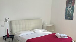Een net opgemaakt bed met een rode deken en witte kussens, een nachtkastje met een lamp en een klein nachtkastje.
