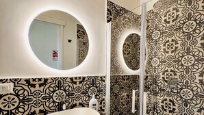 Een badkamer met een ronde spiegel, een wastafel en een douche.