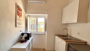 Een kleine keuken met een raam, witte kastjes en een kleine koelkast.
