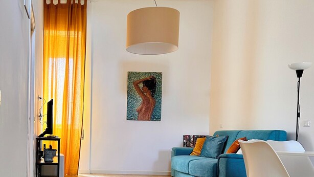 Een moderne woonkamer met een blauwe bank, een witte stoel, een houten vloer, een rood en zwart tapijt, een schilderij aan de muur en een plafondlamp.