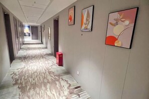 Et hotelværelse med et mønstret tæppe, indrammet kunst på væggene og en rød genstand på gulvet.
