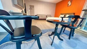 Ett modernt hotellrum med en säng, två svarta stolar, ett litet bord och en blå matta.
