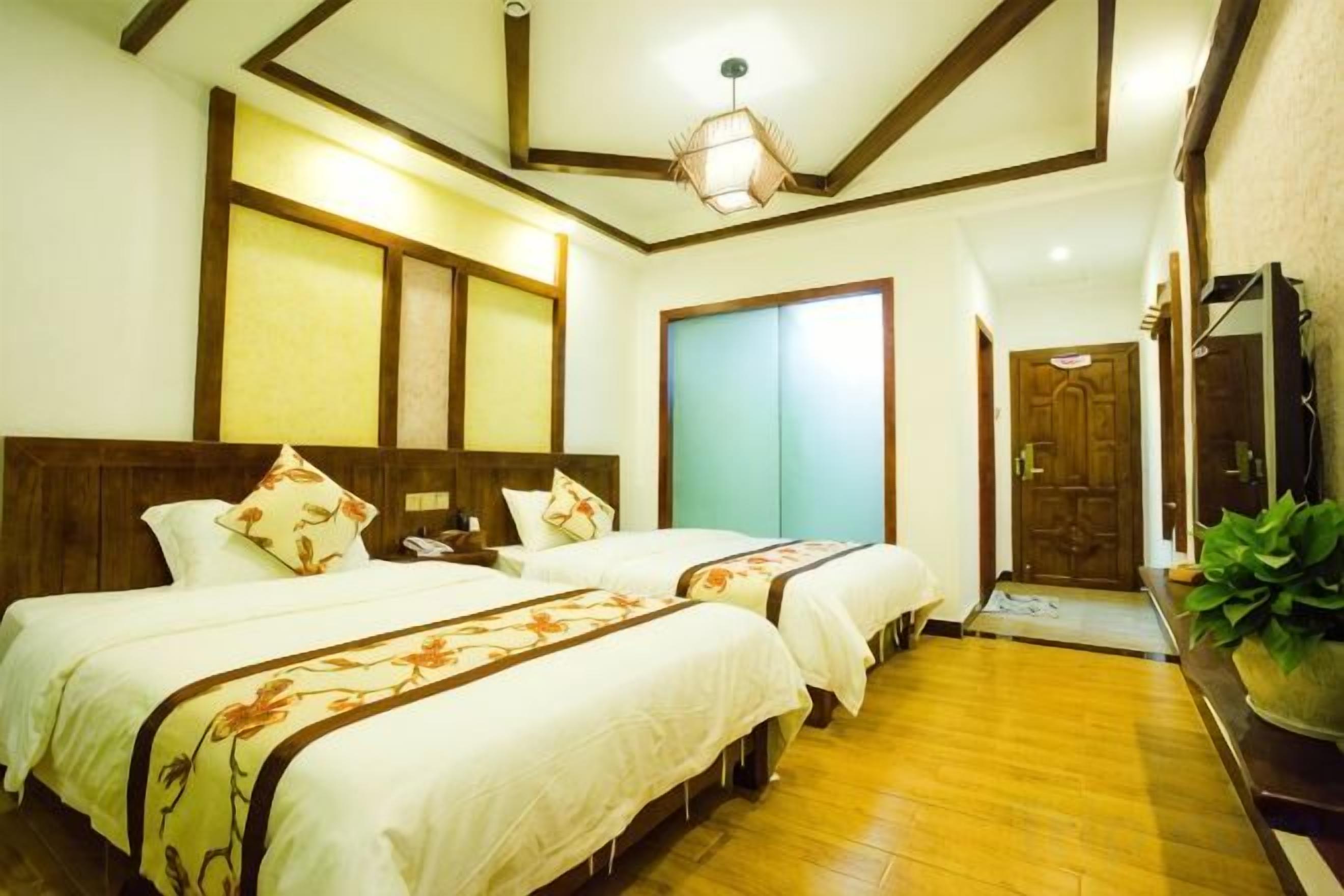 A hotel room with two beds, a wooden floor, a large mirror, and a door leading to another room.