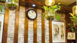 A wall with a clock, stone paneling, wooden beams, hanging plants, and a framed painting. - Jinhua Inn (Zhangjiajie)