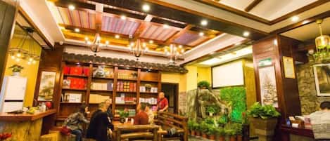 Interior de restaurante con mobiliario de madera, luces colgantes y un adorno de pared verde.