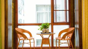 A corner room with a large window, two wicker chairs, a small round table, and a potted plant.