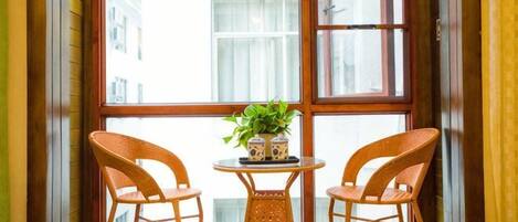 A corner room with a large window, two wicker chairs, a small round table, and a potted plant.