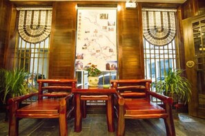 A traditional wooden interior with a central table and chairs, large windows with decorative curtains, and potted plants. - Jinhua Inn (Zhangjiajie)