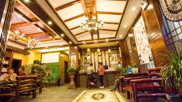 A hotel lobby with a reception desk, seating area, and decorative plants.