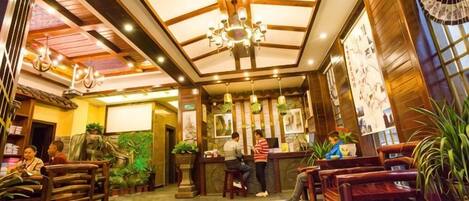 A hotel lobby with a reception desk, seating area, and decorative plants.