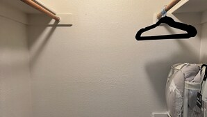 A laundry room with a white wall, wooden floor, a white laundry basket, and a hanging clothes rack.