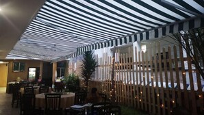 Un espace extérieur aménagé pour les repas, avec des auvents à rayures, des clôtures en bois et des tables.
