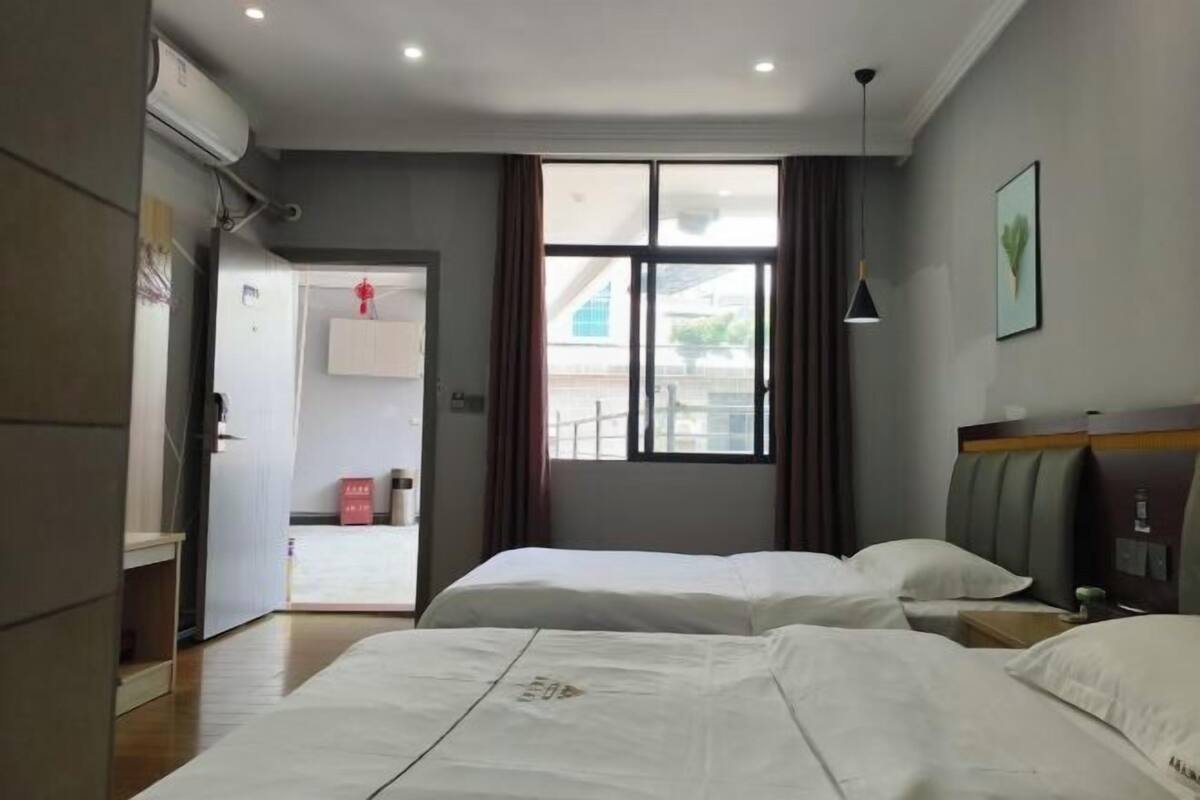 Ein Hotelzimmer mit zwei Betten, einem Fenster mit Vorhängen, einem Nachttisch und einem Kleiderschrank.