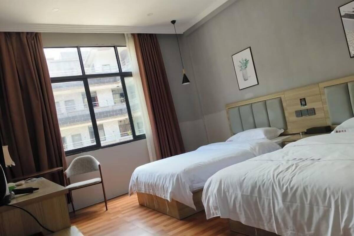 Ein Hotelzimmer mit zwei Betten, einem Schreibtisch, einem Stuhl und einem großen Fenster mit Vorhängen.