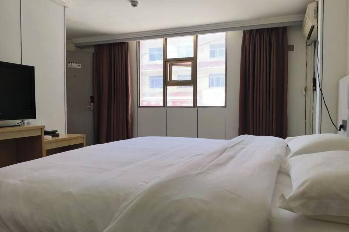 Ein Hotelzimmer mit einem Bett, einem Fernseher auf einem Schrank, einem Fenster mit Vorhängen und einer Wand-Klimaanlage.