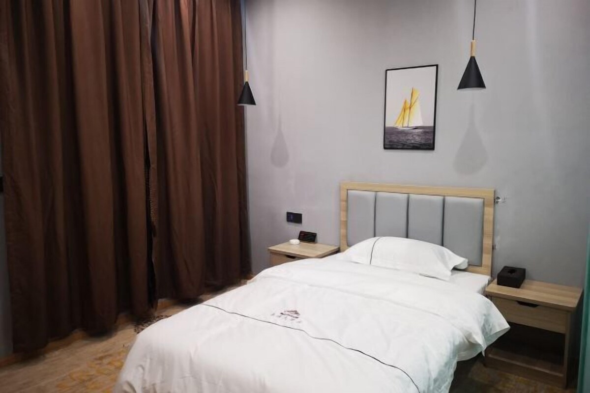 A bedroom with a bed, nightstands, a wooden headboard, a painting, and brown curtains.