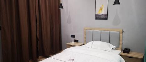 Un dormitorio con cama, mesitas de noche, cabecero de madera, un cuadro y cortinas marrones.