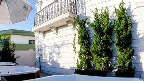 Zona de piscina con un edificio blanco, un balcón y vegetación.