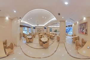 A spacious hotel lobby with multiple seating areas, a central chandelier, and a view of the dining area.