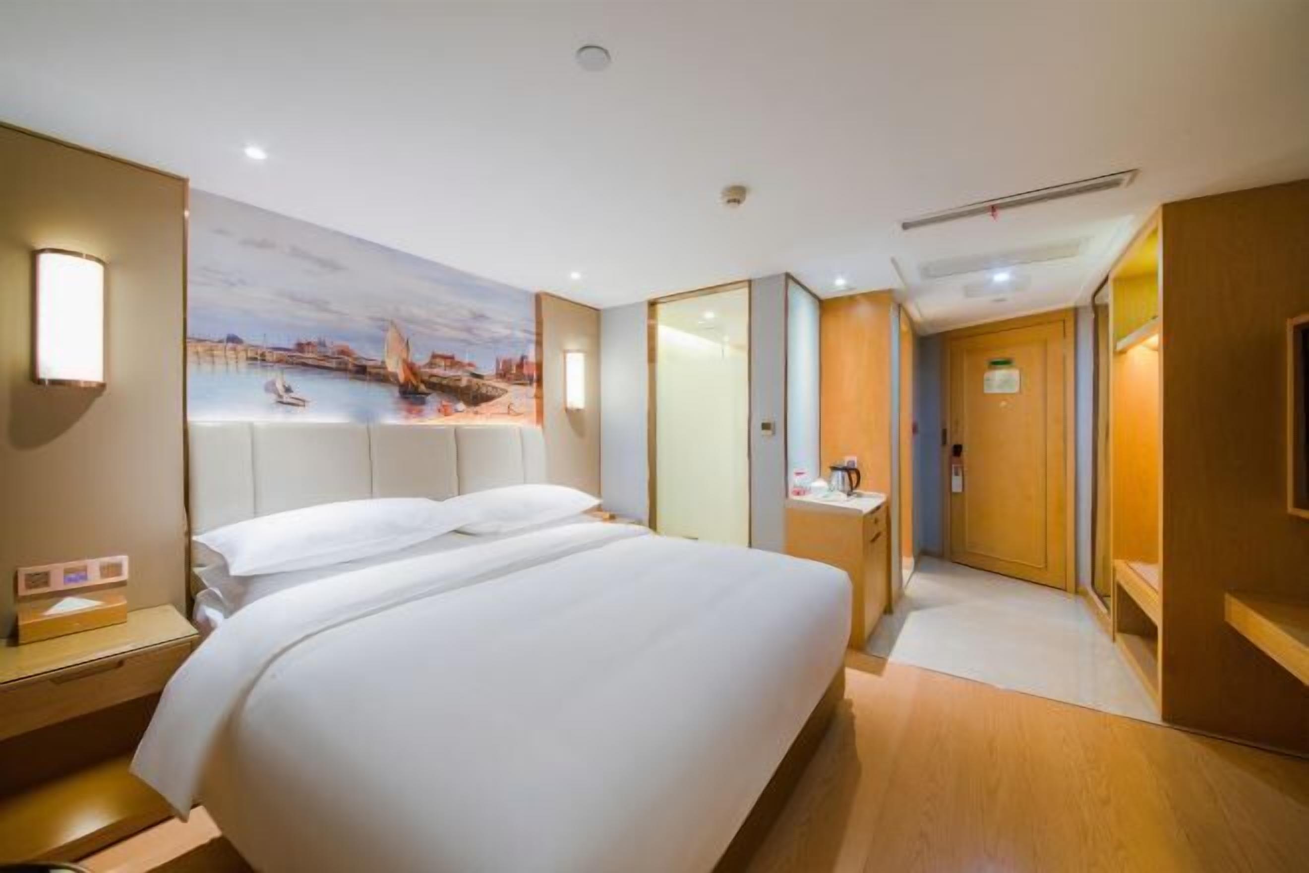 Une chambre d’hôtel avec un lit, une table de chevet, un bureau, une chaise, un tableau et une porte.