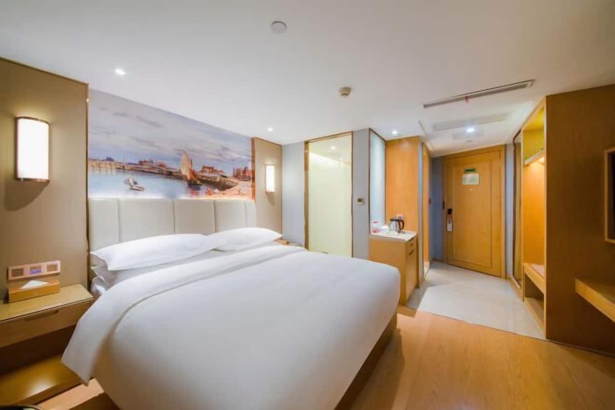 Ein Hotelzimmer mit Bett, Nachttisch, Schreibtisch, Stuhl, einem Gemälde und einer Tür.