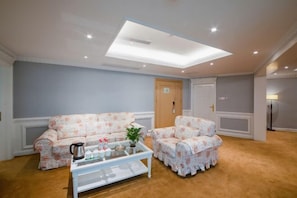 A living room with a sofa, armchair, coffee table, and a ceiling light fixture. - Vienna International Hotel (Wanzhou Gaosuntang Pedestrian Street Branch) (Chongqing)