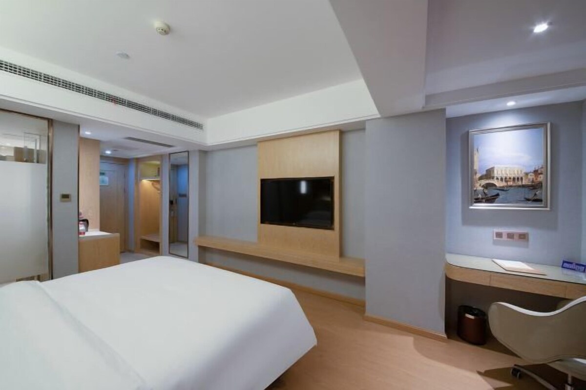 A hotel room with a bed, a desk, a TV, and a framed picture on the wall.