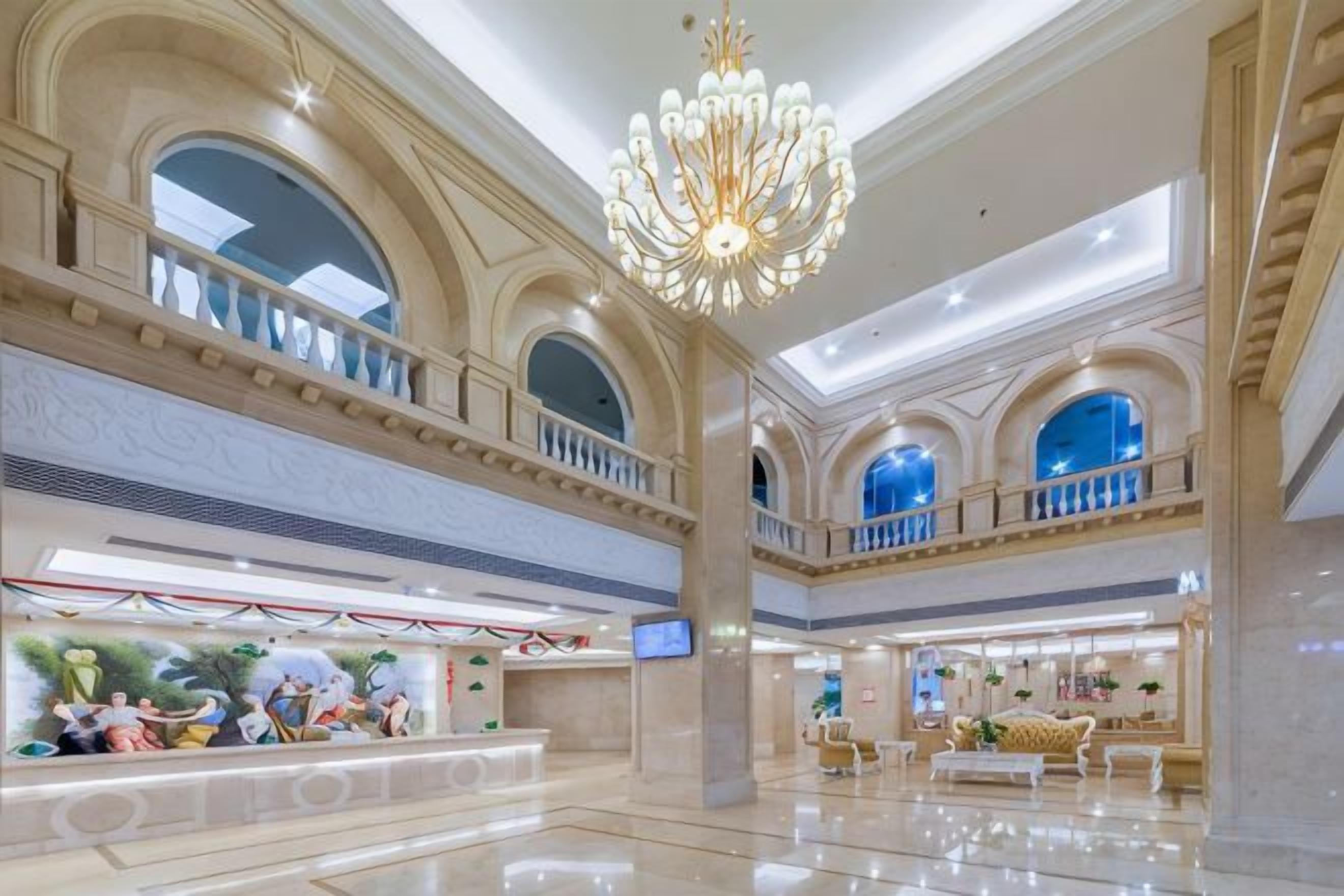 A spacious lobby with a high ceiling, a grand chandelier, and a reception area with a digital display.