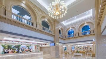 A spacious lobby with a high ceiling, a grand chandelier, and a reception area with a digital display.