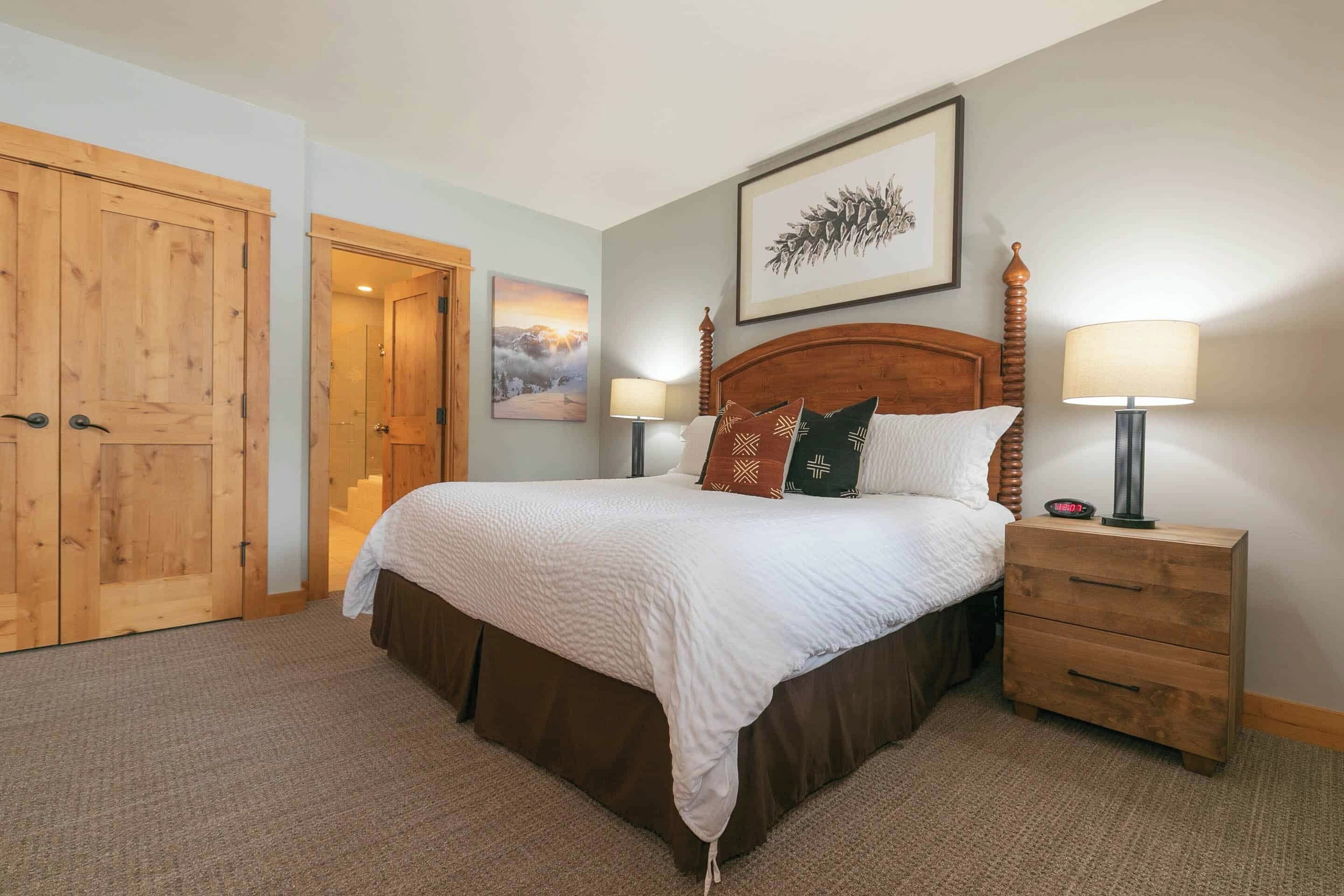A bedroom with a large bed, wooden wardrobe, and a nightstand with lamps.
