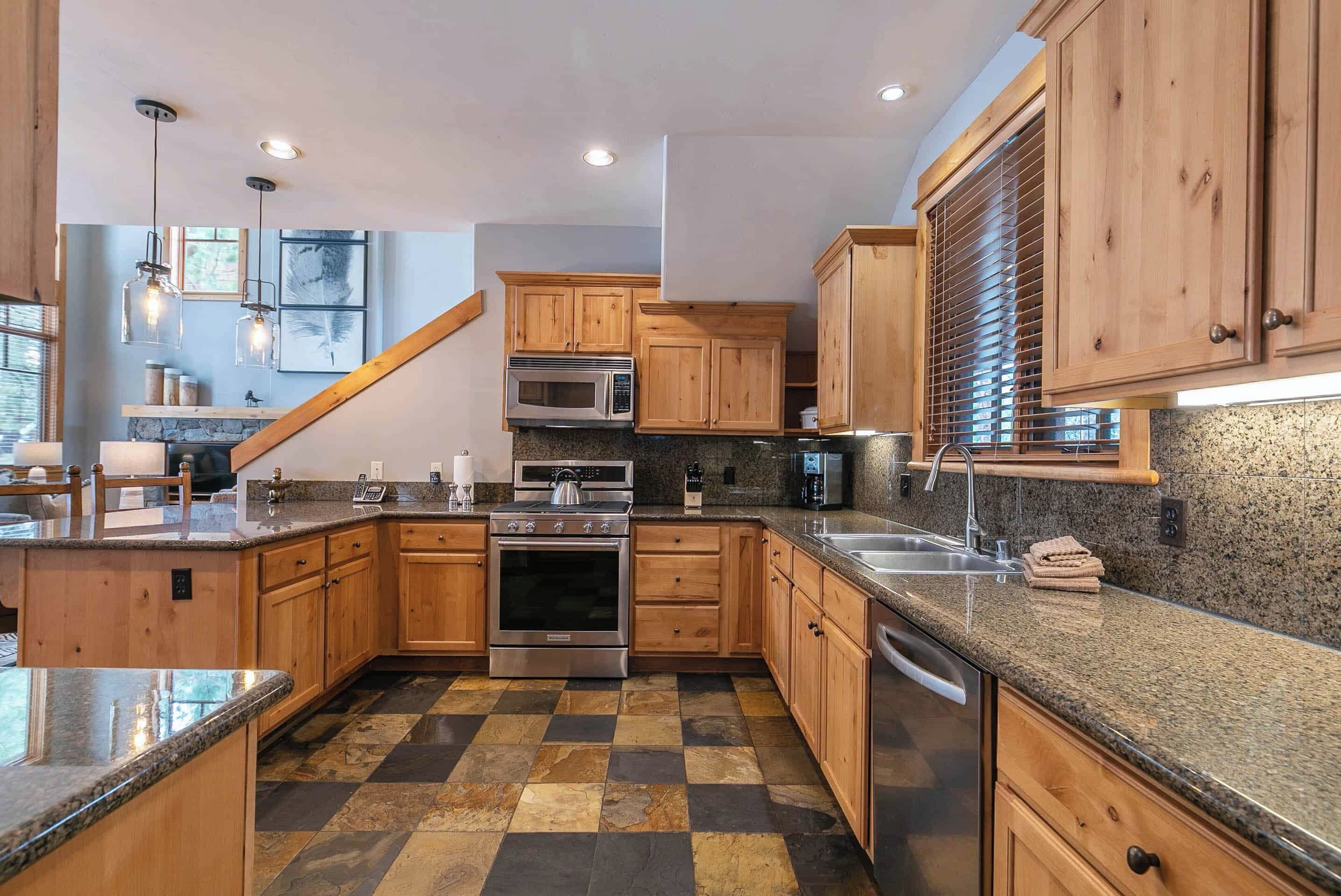 A modern kitchen with wooden cabinets, granite countertops, stainless steel appliances, and a checkered floor pattern.