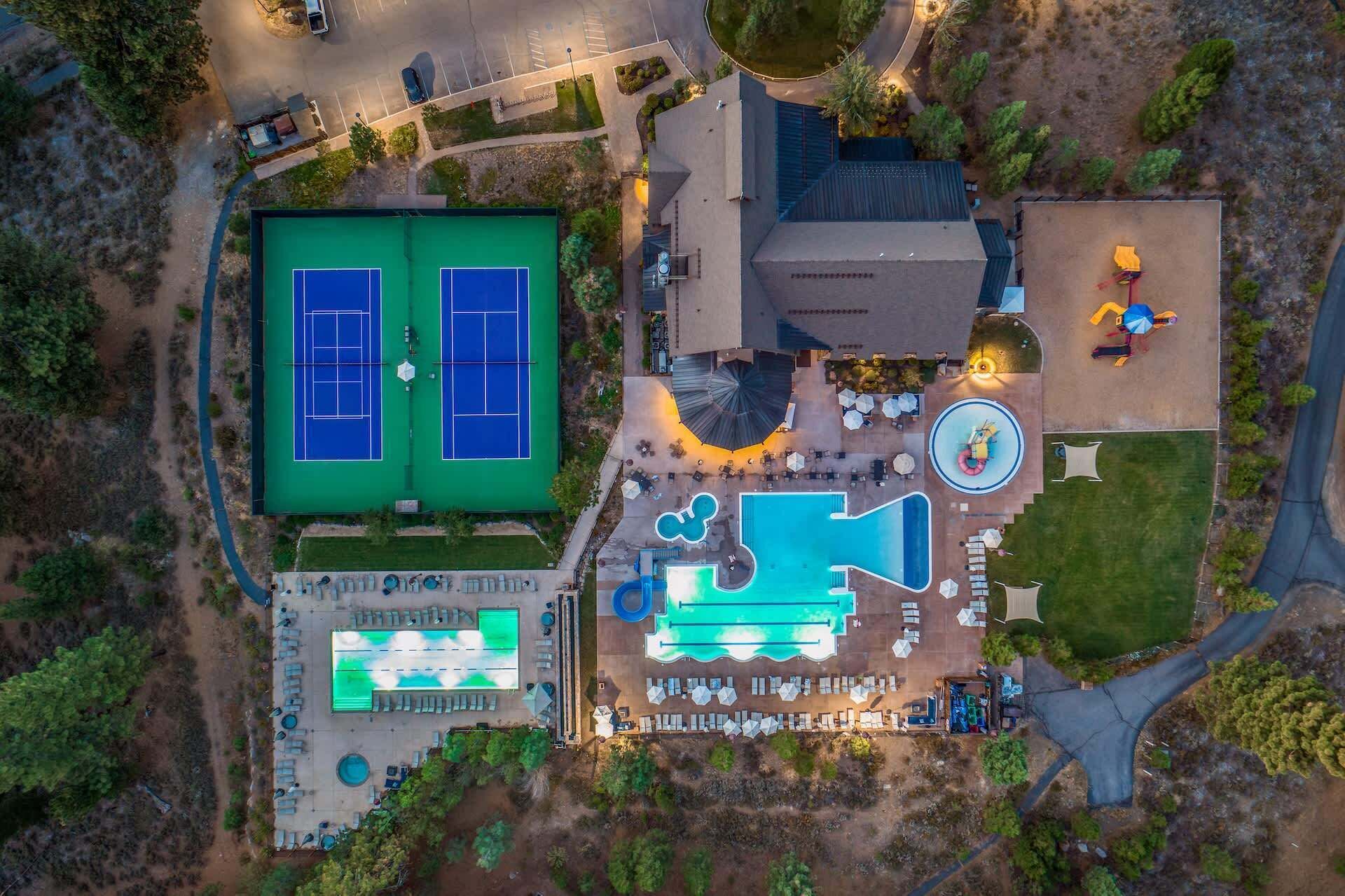An aerial view of a resort with tennis courts, a swimming pool, and outdoor seating areas.