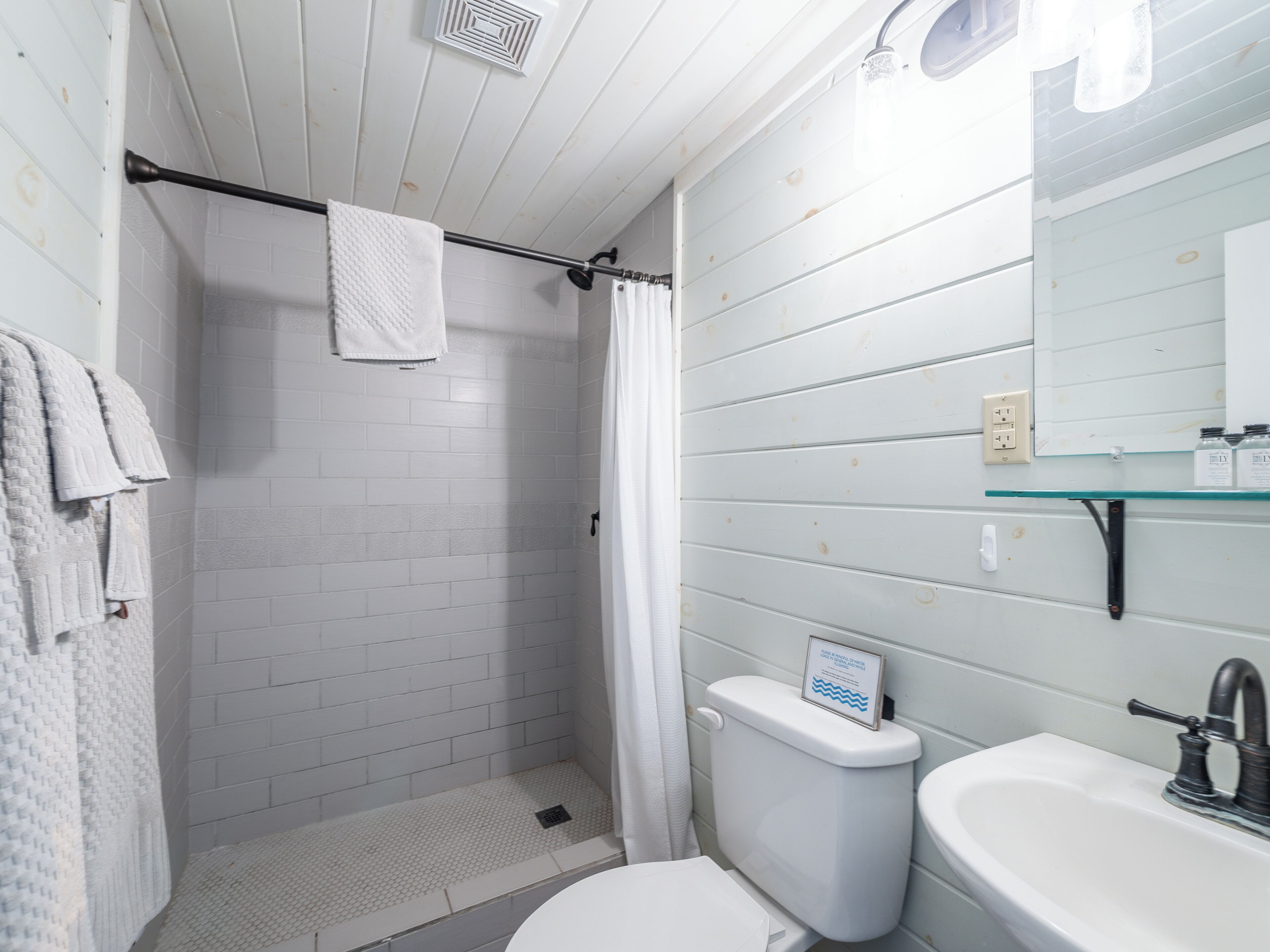A bathroom with a shower, toilet, sink, and a glass shelf with toiletries.
