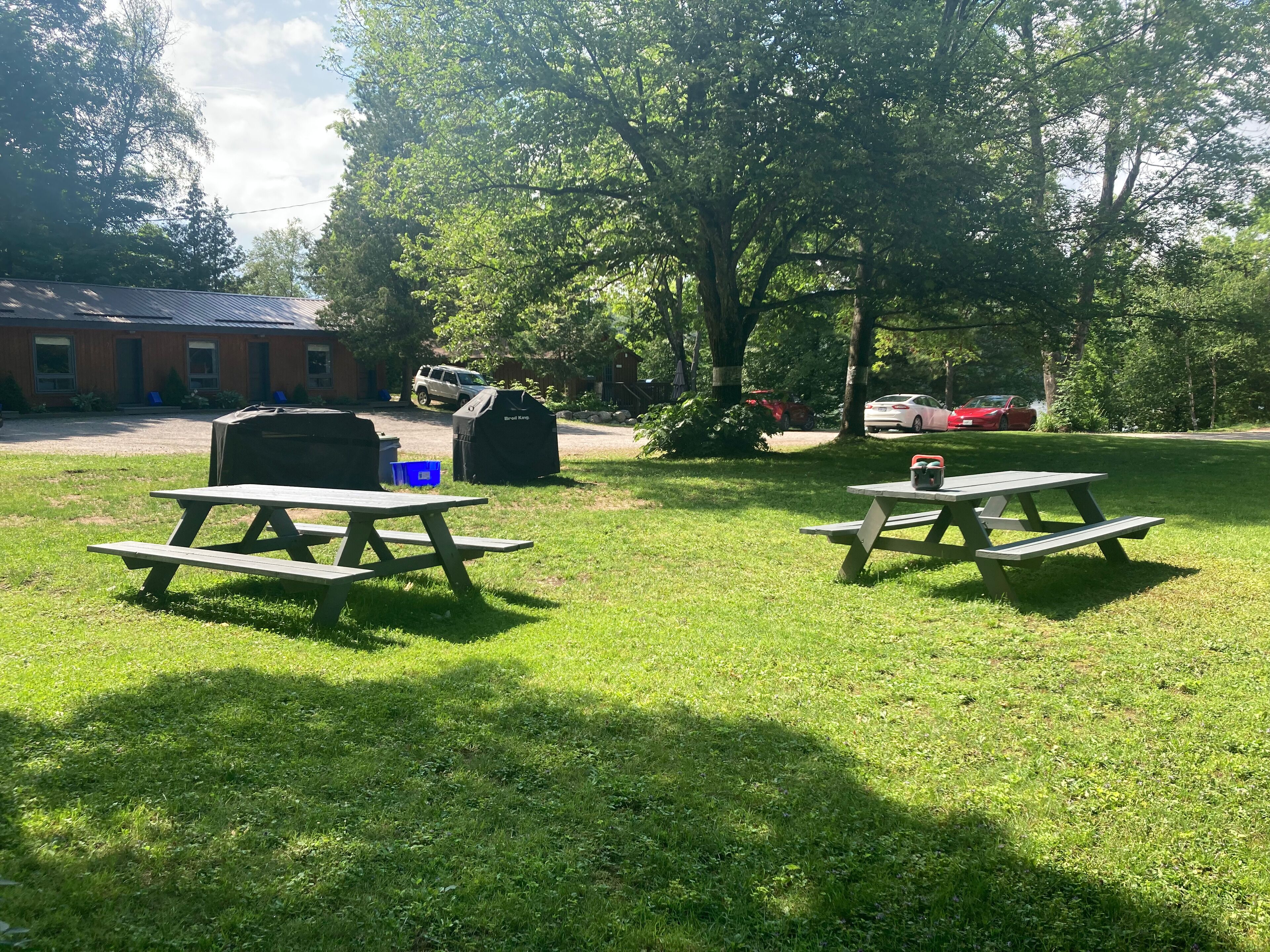 Two picnic tables in a grassy outdoor area with a brick building in the background.