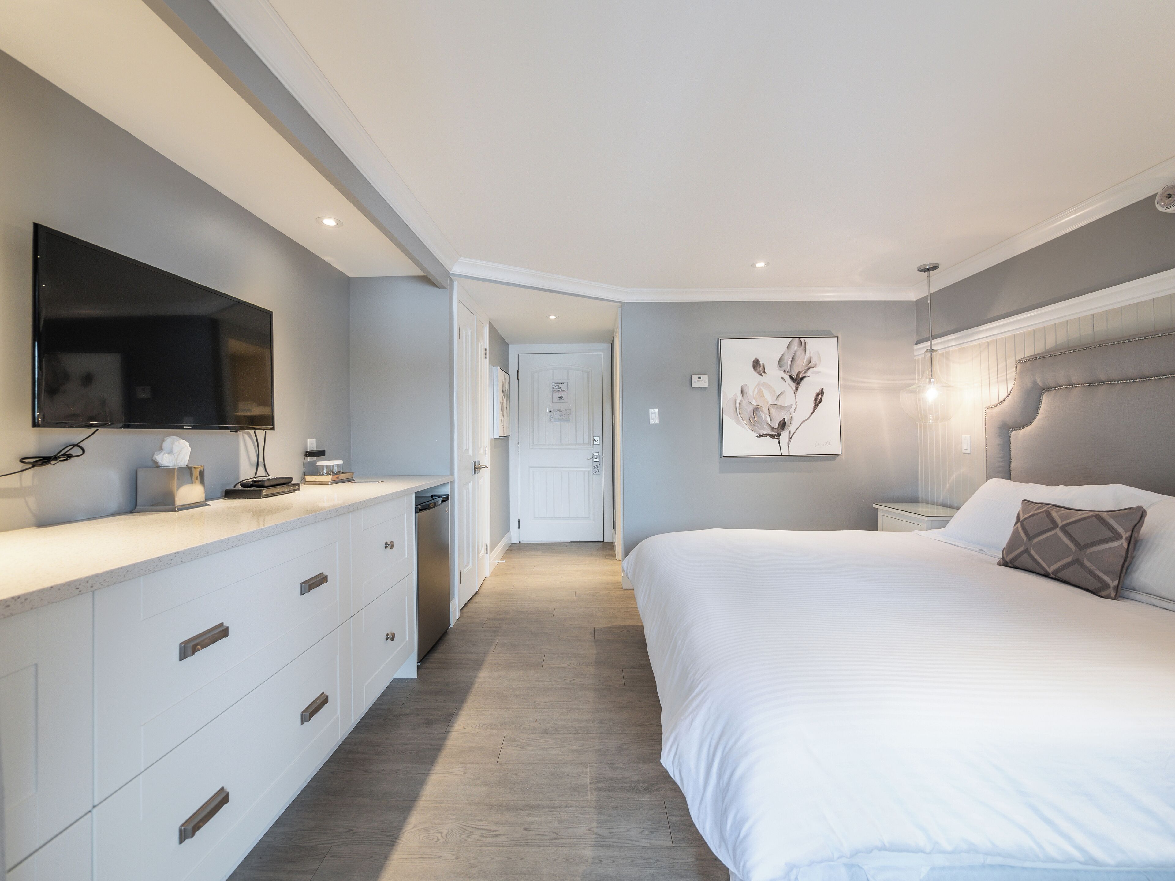 A modern bedroom with a large bed, bedside tables, a flat-screen TV, and a door leading to another room.