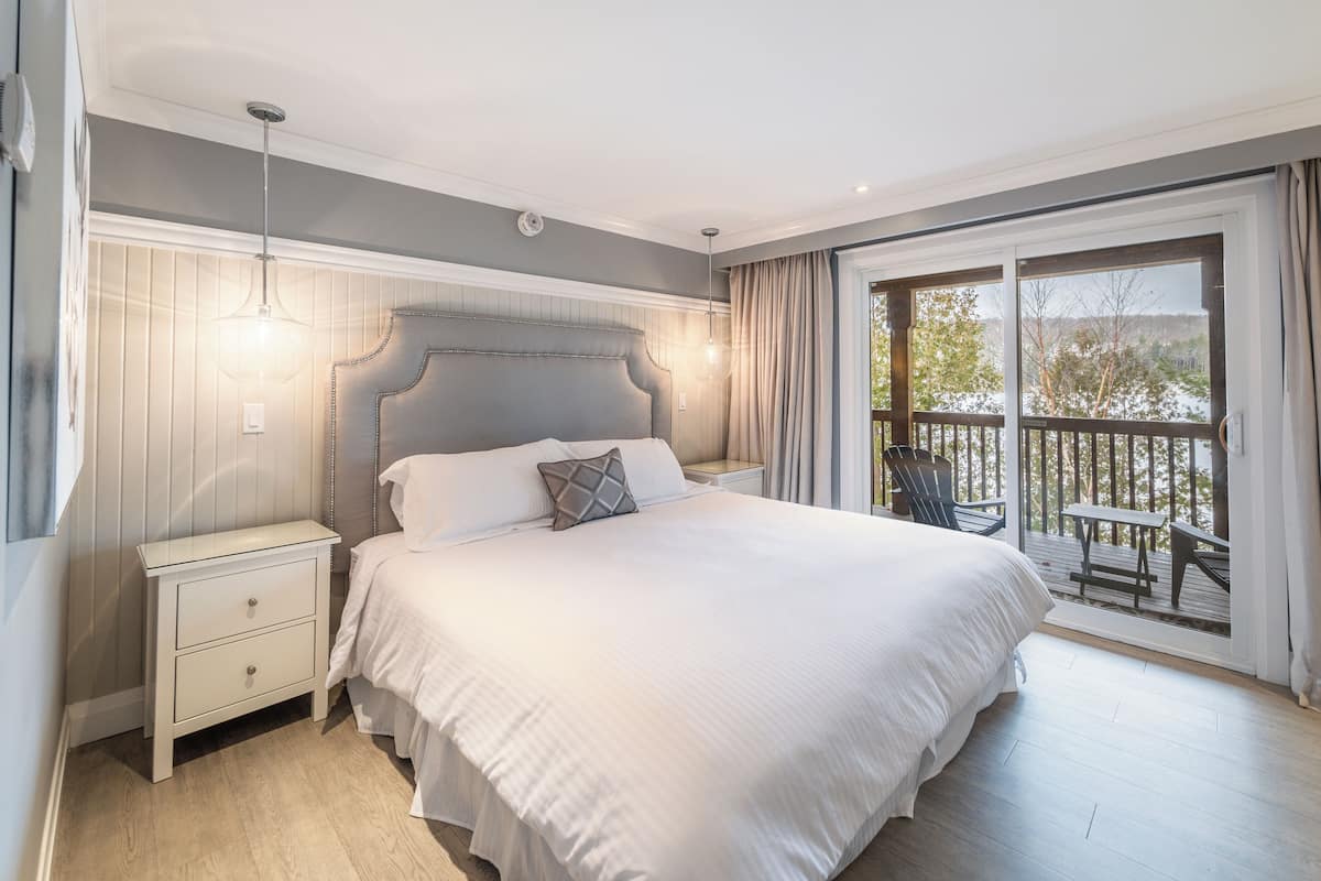 A bedroom with a large bed, a nightstand, a dresser, and a view of a balcony with outdoor furniture.