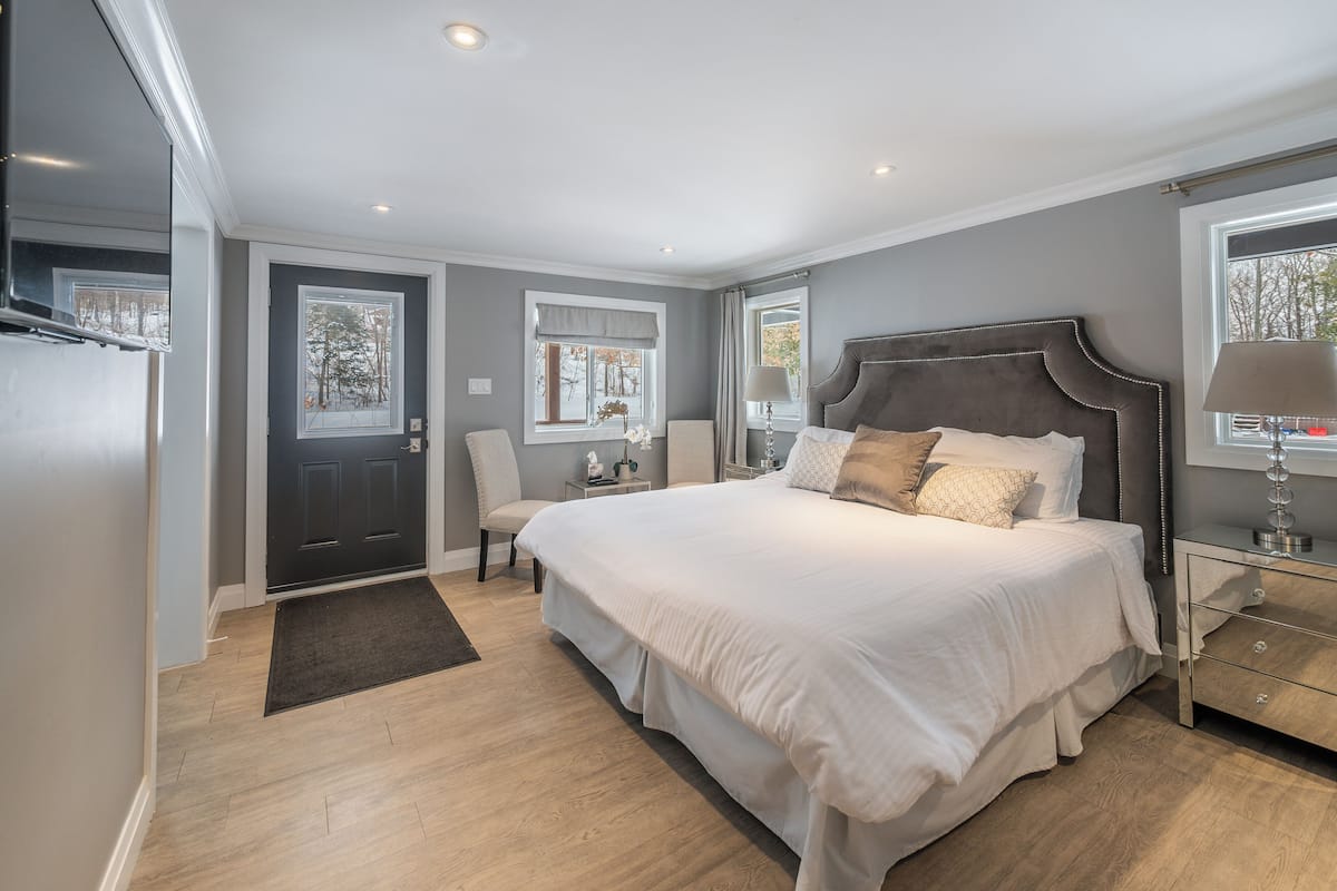A bedroom with a large bed, a nightstand, a chair, a window, and a door.