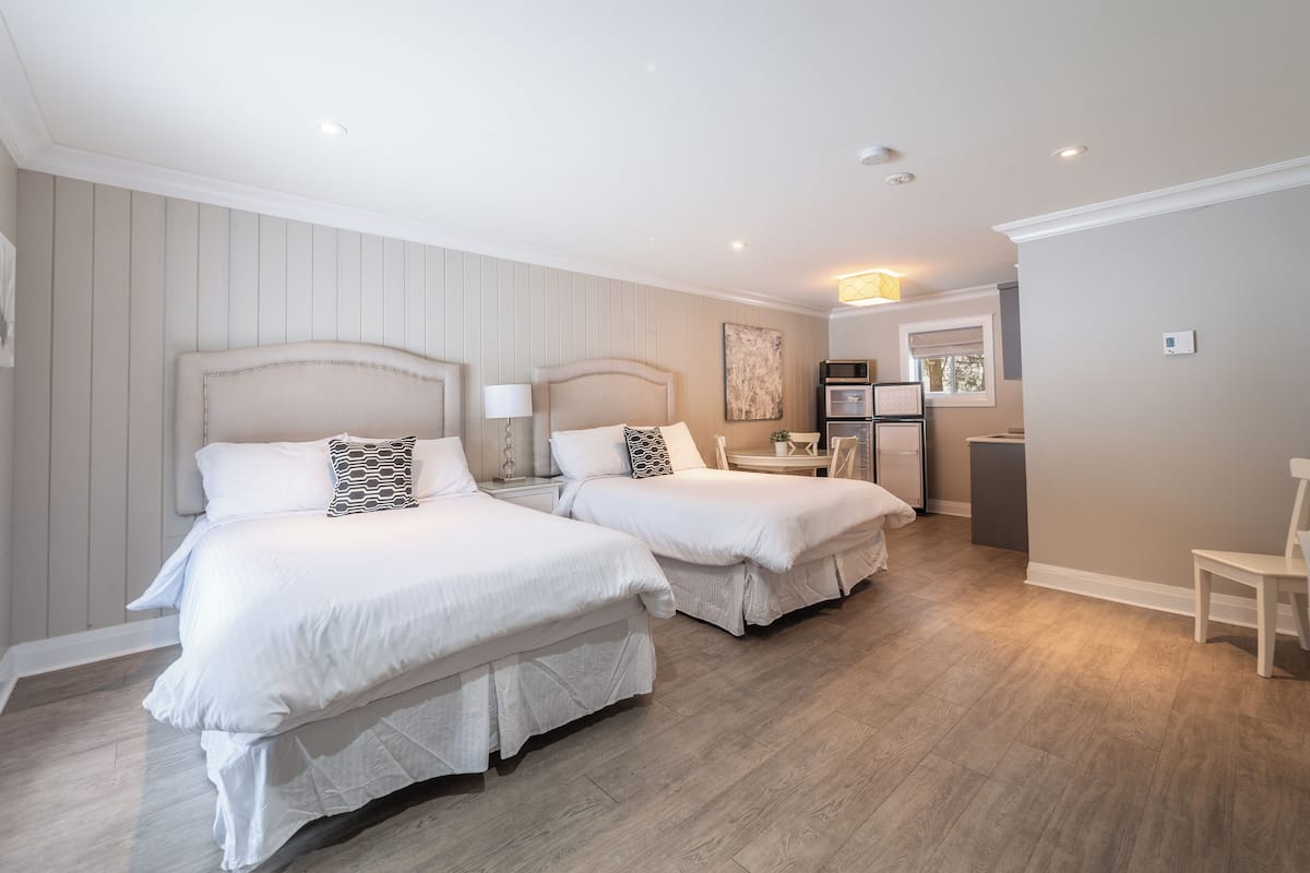 A hotel room with two beds, a small kitchenette, and a dining area.