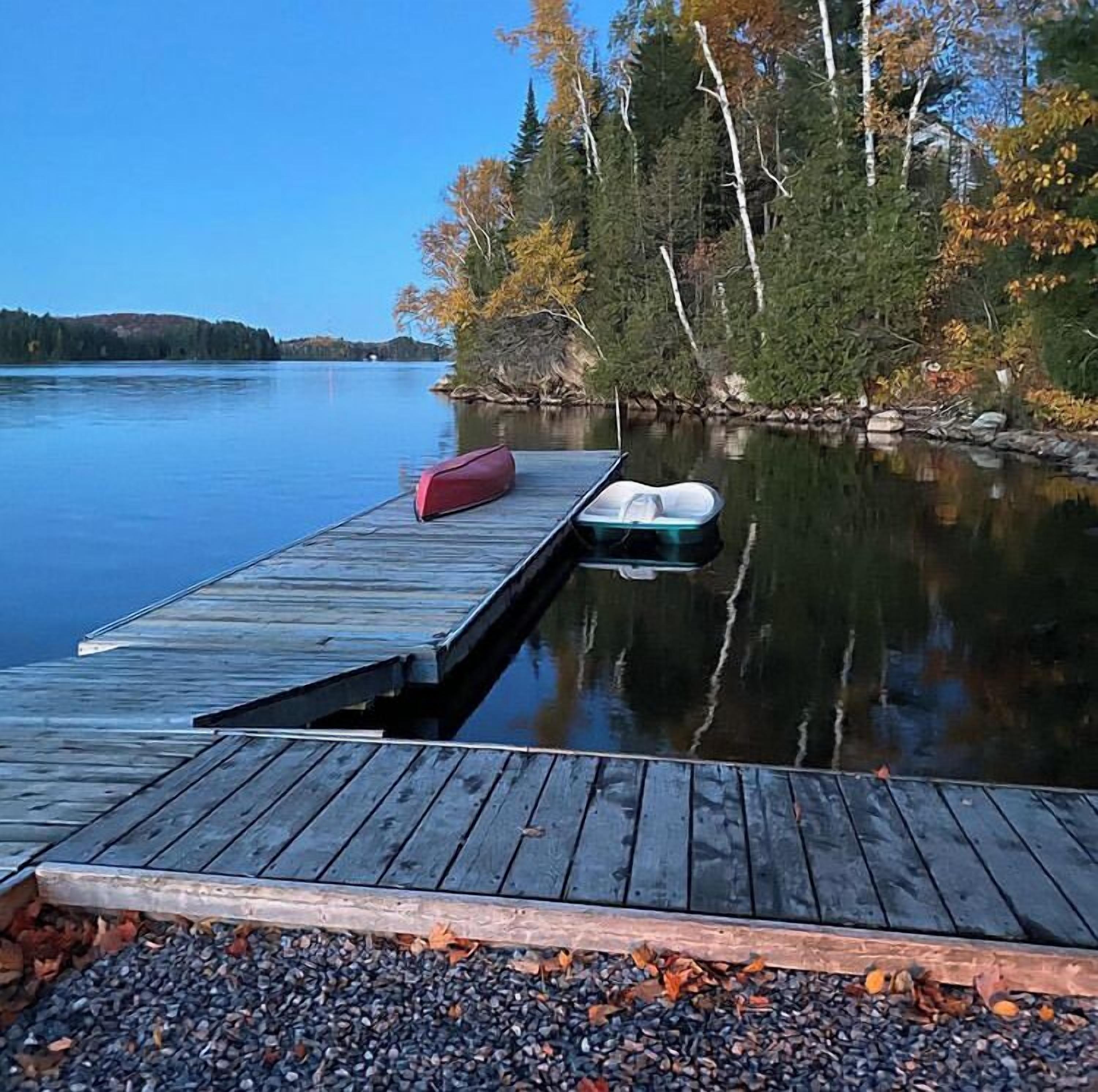 A wooden dock extending into calm water, with a red and a white canoe on it.