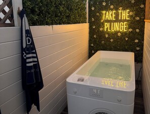 Ein Wellnessbereich mit Whirlpool, Handtuchhalter und Handtuch, sowie einem Neon-Schild mit der Aufschrift 'TAKE THE PLUNGE'.