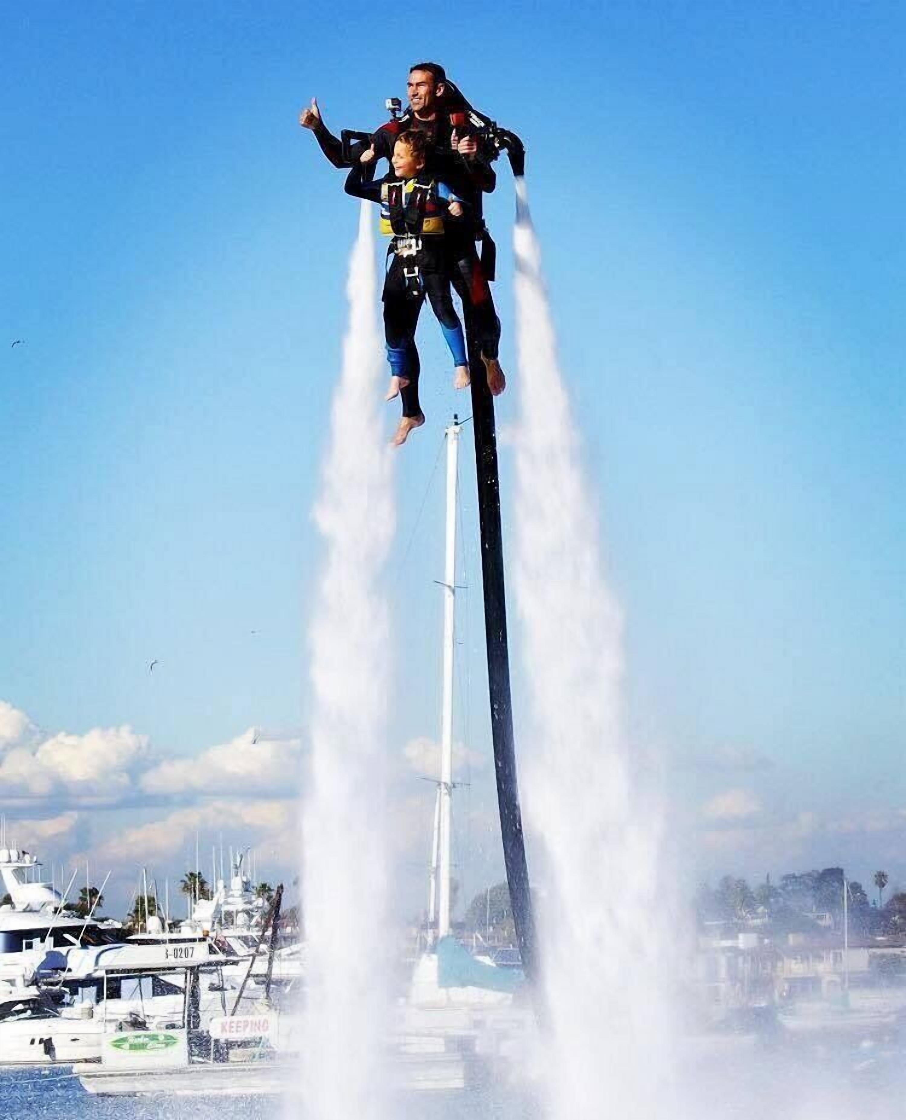 A person performing a high-flying stunt on a jet ski, with water jets creating a vertical column behind them.
