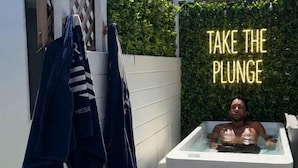 Une personne dans un bain à remous, avec un mur de verdure en arrière-plan et un panneau indiquant : « Lancez-vous ! ».