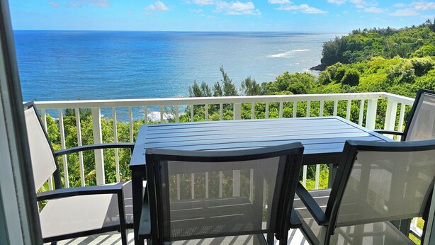 A balcony with a table and chairs overlooking a coastal view.