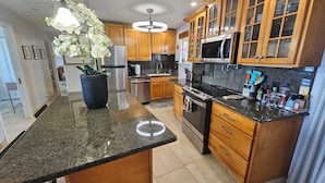 A kitchen with granite countertops, wooden cabinets, stainless steel appliances, and a potted orchid.
